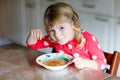 Adorable little toddler girl eating fresh cooked vegetable soup in kitchen. Happy child eats healthy food for lunch or
