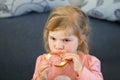 Adorable little toddler girl eating fresh prepared salami sandwith in kitchen. Happy child eats healthy food for lunch