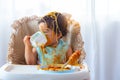 Adorable little toddler girl or infant baby drink water after eat delicious spaghetti food on chair. Funny cute infant girl get Royalty Free Stock Photo