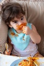 Adorable little toddler girl or infant baby eating delicious food with tomato sauce and sucking thumb, finger. Funny cute infant Royalty Free Stock Photo