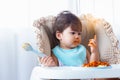 Adorable little toddler girl or infant baby eating delicious spaghetti food with tomato sauce on baby chair. Cute infant girl Royalty Free Stock Photo