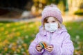 Adorable little toddler girl with medical mask and painted rainbow on stone during pandemic coronavirus quarantine. Cute Royalty Free Stock Photo