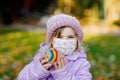 Adorable little toddler girl with medical mask and painted rainbow on stone during pandemic coronavirus quarantine. Cute Royalty Free Stock Photo