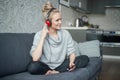 Adorable middle aged blond woman sitting on sofa in her home and listen to the music