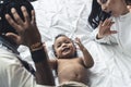 Adorable mixed-race infant laying down, playing with parents, and smiling.