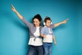 Adorable mother and daughter wearing headphones, equally dressed singing and dancing against a blue background with copy space Royalty Free Stock Photo