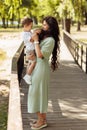 Adorable mother with joyful son at the park, beautiful woman hold in arms little boy, smiling, mommy plays with kid