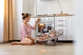 Adorable mother wearing casual striped shirt and short sitting on floor with toddler daughter in rocking chair, sets the Royalty Free Stock Photo