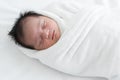 Adorable newborn baby wrapped in white swaddle towel lying on bed and sleeping peacefully. Sleeping cute infant in a wrap on white Royalty Free Stock Photo