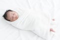 Adorable newborn baby wrapped in white swaddle towel lying on bed and sleeping peacefully. Cute infant in a wrap on white blanket Royalty Free Stock Photo