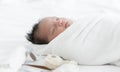 Adorable newborn baby wrapped in white swaddle towel lying on bed and sleeping peacefully with dolls. Cute infant in a wrap on Royalty Free Stock Photo