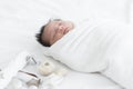 Adorable newborn baby wrapped in white swaddle towel lying on bed and sleeping peacefully with dolls. Cute infant in a wrap on Royalty Free Stock Photo