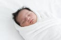 Adorable newborn baby wrapped in white swaddle towel lying on bed and sleeping peacefully. Sleeping cute infant in a wrap on white Royalty Free Stock Photo