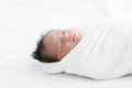 Adorable newborn baby wrapped in white swaddle towel lying on soft bed and sleeping peacefully. Sleeping infant in a wrap on white Royalty Free Stock Photo