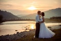 Adorable newlywed couple is gently kissing on the river bank during the sunset. Royalty Free Stock Photo