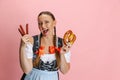 Adorable Oktoberfest woman, waitress wearing a traditional Bavarian or german dirndl holding bretzel  on pink Royalty Free Stock Photo