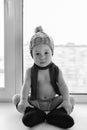 Adorable one year old baby boy lonely sitting on the windowsill weared in winter hat, shoes and scarf, indoors. Royalty Free Stock Photo