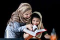 Adorable Pakistani girl with beautiful eyes wear hijab, learning Quran book with mother, Muslim family, daughter and mom read holy Royalty Free Stock Photo