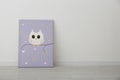 Adorable picture of owl on floor near white wall, space for text. Children`s room interior element