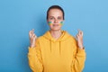 Adorable positive hopeful woman wearing hoodie with blue and yellow flag on cheeks, standing isolated over blue background and