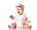 Adorable positive little baby girl in white body, hair bow decoration sitting on floor, smiling and holding brush in hand