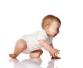 Adorable positive little baby infant in white cotton body and barefoot trying to creep on floor, smiling and looking aside