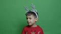 Adorable preschool child boy in red sweater and deer antlers winking. isolated on greens background.