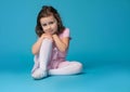 Adorable preschool girl child, ballet dancer, posing to the camera, sitting over blue background