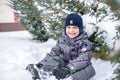 Adorable preschooler in winter wear sit amoung snow and play wit