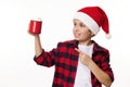 Adorable preteen boy in Santa hat, pointing on a red mug of hot chocolate and marshmallows, isolated on white background Royalty Free Stock Photo