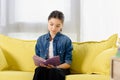 adorable preteen child sitting on yellow sofa and reading book