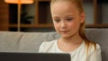 Adorable preteen little girl sitting on couch using modern laptop to watch cartoon movie funny video looking at computer Royalty Free Stock Photo