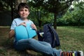 Adorable preteen schoolboy holding copybook, relaxing in a park after class, smiles cutely looking at camera. Royalty Free Stock Photo