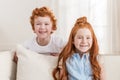 Adorable redhead sister and brother sitting together on sofa at home