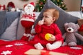 Adorable redhead toddler sucking christmas star decoration sitting on sofa at home