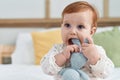 Adorable redhead toddler sucking doll sitting on bed at bedroom