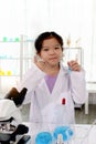 Adorable schoolgirl in lab coat doing simple science experiments, young Asian kid scientist holding tube and giving thumbs up Royalty Free Stock Photo