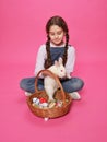 Adorable schoolgirl plays with cute bunny, puts them in a basket, poses in the studio, on a pink background. Royalty Free Stock Photo