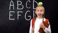 Adorable schoolgirl standing with apple on head, having good idea, smart kid Royalty Free Stock Photo