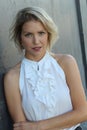 Adorable shapely blond woman in classy white silk blouse posing on gray background