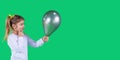Adorable shiny young girl holding a dark green balloon in front of her and thinking to whom to give it. Royalty Free Stock Photo