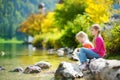 Adorable sisters playing by Konigssee lake in Germany on warm summer day. Cute children having fun feeding ducks and throwing ston