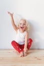 Adorable small female child wears pyjamas, sits on wooden floor raises hands as happy to see affectionate parents