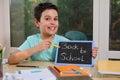 Adorable smart schoolboy points with pencil on a chalkboard with inscription Back To School. New academic year semester