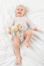 Adorable smiling baby boy with blue eyes lying on a bed with his favourite stuffed teddy bear toy, looking at camera. Royalty Free Stock Photo