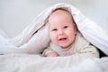 Adorable smiling baby boy under white blanket in bedroom. Newborn child relaxing in bed. Family morning at home. New Royalty Free Stock Photo