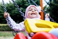 Adorable smiling baby girl with kerchief enjoying a swing ride on a playground in a park on a nice sunny summer day Royalty Free Stock Photo