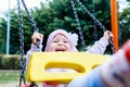 Adorable smiling baby girl with kerchief enjoying a swing ride on a playground in a park on a nice sunny summer day Royalty Free Stock Photo