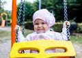 Adorable smiling baby girl with kerchief enjoying a swing ride on a playground in a park on a nice sunny summer day Royalty Free Stock Photo