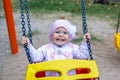 Adorable smiling baby girl with kerchief enjoying a swing ride on a playground in a park on a nice sunny summer day Royalty Free Stock Photo